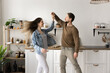 © fizkes - Young attractive couple in love dancing together in modern domestic kitchen, holding hands, swirling, enjoy carefree pastime, moving to popular track. Romantic couple rehearsing wedding dance at home