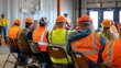 © Copi - A group of construction workers are sitting in chairs and listening to a safety briefing. They are all wearing hard hats and safety vests.
