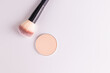 © Marina - A round block of compact powder in a natural tone on a white background with a large fluffy brush for applying makeup. top view. space for text