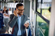 © Drazen - Happy businessman using cell phone while listening music over earphones in city bus.