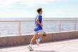 © muse studio - Man in blue and white shirt running along a waterfront, enjoying a sunny day by the sea.