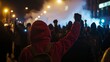 © Vitezslav Vylicil - Crowd of protesters with raised fists walking in a march at night, lit by street lamps, rioter in a red hoodie in the foreground, activism and demonstration concept.