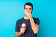 © luismolinero - Young man with a cornet ice cream over isolated blue background covering mouth with hands