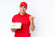 © luismolinero - Pizza delivery caucasian man with work uniform picking up pizza boxes isolated on white background pointing to the side to present a product