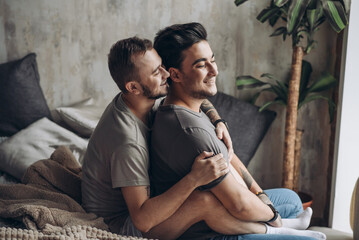 Wall Mural - Two homosexual male partners taking care of each other. Lovely gay couple have warm cuddle, having fun in bed and smile joyfully, feeling free and natural in same-sex conduct.