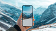© wuttichai1983 - A hand holding a smartphone, framing a picturesque mountain scene in the background.