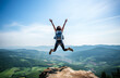 © Minimal Blue - Excited woman with arms raised, celebrating on a mountain peak with a beautiful landscape