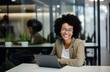 © Minimal Blue - Smiling businesswoman with glasses sitting at a desk in a modern office, using a laptop