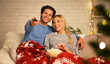 © Prostock-studio - Christmas eve. Loving couple watching tv and eating popcorn at home, covered with blanket
