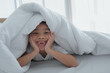 © Anatta_Tan - Asian boy smiles toothlessly lying on the bed under the blanket She is having fun posing for pictures