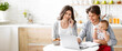 © Prostock-studio - A young couple works from home in their kitchen. The woman is on a phone call, while the man is working on a laptop, holding their baby on his lap. The baby is looking at the laptop screen