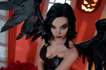 A woman in a black and red Halloween costume with black wings, standing indoors with a jack-o'-lantern in the background