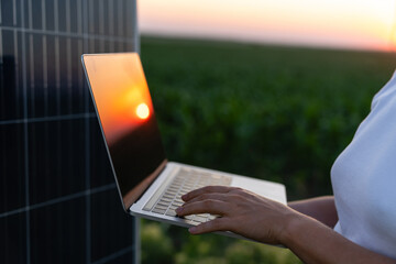 Wall Mural - Woman farmer with laptop stands next to solar panel