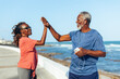 © (JLco) Julia Amaral - Senior couple high fiving by the seaside celebrating fitness achievements