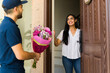 © AntonioDiaz - Woman smiling as she receives a flower bouquet from a delivery person at the doorstep of her home