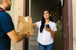 © AntonioDiaz - Happy customer receiving a food order at home from a delivery man using a smartphone app
