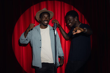 Wall Mural - Duet two happy friends African American mans speaking to microphone performing in comedy show open mike stand up on stage with red curtains