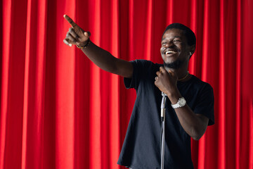 Wall Mural - African american man comic with old microphone on theater stage on red curtains background. Concept banner standup comedian show