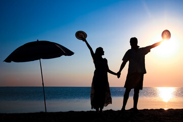 Wall Mural - A Happy couple by the sea at sunset on travel silhouette in nature