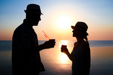 Wall Mural - A Happy couple drinking cocktail by the sea at sunset on travel silhouette in nature