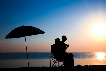 Wall Mural - A Happy couple by the sea at sunset on travel silhouette in nature