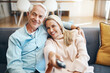 © Penn/peopleimages.com - Mature couple, sofa and watching tv together for news, streaming movies and bonding in home. Lounge couch, man and woman with remote for television broadcast, change channel and series subscription