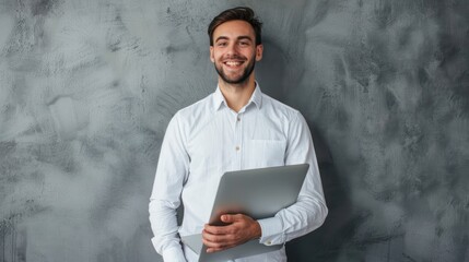 Portrait happy smiling young businessman in white shirt holding laptop grey background