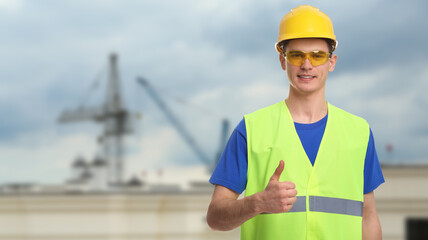 Wall Mural - Young man wearing safety equipment and showing thumbs up at construction site. Banner design with space for text