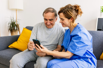 Friendly caregiver teaching her patient how to use a mobile phone during weekly visit at home. Elderly lifestyle and technology concept