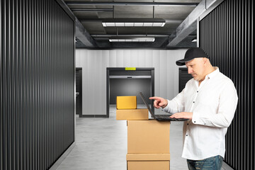 Wall Mural - Self storage unit. Man in building with personal warehouses. Open storage unit behind person. Man brought boxes to warehouse. Guy uses laptop to rent self storage unit. Corridor with warehouse spaces