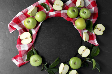 Wall Mural - Ripe green apples, leaves and towel on black textured table, flat lay. Space for text