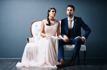 Bride, groom or together in studio on chair for marriage, stress or concerned for wedding. People, couple or blue background with hand holding for commitment with fear, anxiety or mistake in Chicago