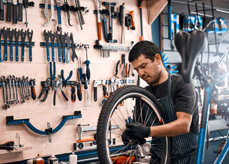 Bike repair, maintenance and wheel with man in workshop for frame building or professional engineering. Assessment, bicycle and tools on wall with mechanic or technician in startup for restoration