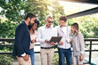 © JorSons/peopleimages.com - Business people, outdoor and cooperation with laptop, creative project and planning with research. Group, employees and leader with staff, tech and online reading for review, feedback and teamwork