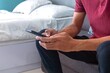 © fadfebrian - A man sitting on a sofa and holding a smartphone in his bedroom