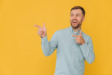 Canvas Print - Cute unshaven man in mint shirt pointing fingers up at copy space isolated on yellow background