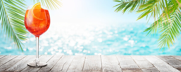 Poster - Glass of Aperol Spritz on a table with a stunning sea and beach background