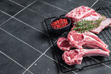 Wall Mural - Fresh Raw lamb meat chop steaks on kitchen table with spices and herbs. Black background. Top view. Copy space