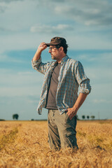 Wall Mural - Male farmer standing in ripe wheat field and looking over the harvest ready crops at the horizon and sunny sky