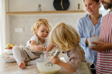 Wall Mural - Young nuclear family making pancakes together. Parents and children in kitchen, preparing pancake batter, spending weekend day indoors.