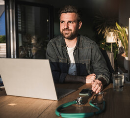 Thoughtful freelancer sitting with laptop at desk