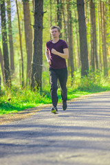 Running man jogging in city park at beautiful summer day. Sport fitness model caucasian ethnicity training outdoor.