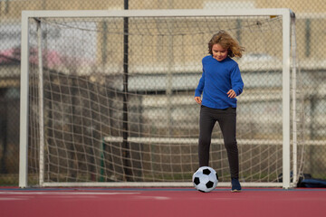 Wall Mural - Child boy football or soccer player in action on stadium kicking football ball for goal. Concept of sport, competition. Kid play football ball. Kid with football ball. Sport, soccer hobby for kids.