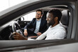 © sofiko14 - Modern car interior visible, professionalism, customer service, and positive buying experience. Caucasian car dealer sit inside vehicle with African American buyer discussing car features and details.