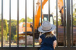 © Austockphoto - Child looking through fence at digger excavator on worksite