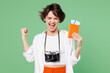 © ViDi Studio - Traveler excited woman wears casual clothes hold passport ticket do winner gesture isolated on plain green background. Tourist travel abroad in free spare time rest getaway. Air flight trip concept.