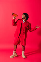 Wall Mural - Young Indian man in vibrant red suit holds a red megaphone against a vivid backdrop.