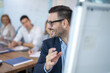© Bojan - Close up of businessman pointing to the whiteboard and smiling while talking to his business partners during presentation in conference room.