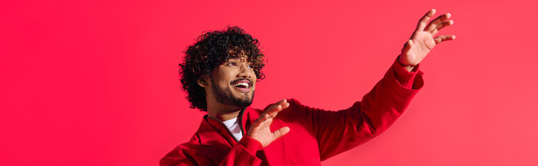 Wall Mural - A handsome young Indian man in a vibrant red jacket strikes a dramatic gesture.