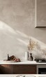 © Nadin Faust - kitchen wall with light gray microcement texture, white marble countertop, beige cabinets, vase of dried flowers, sunlight creating beautiful shadows, simple yet elegant luxury interior design
